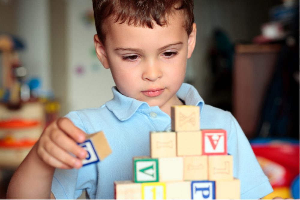 A young child concentrating while stacking alphabet blocks